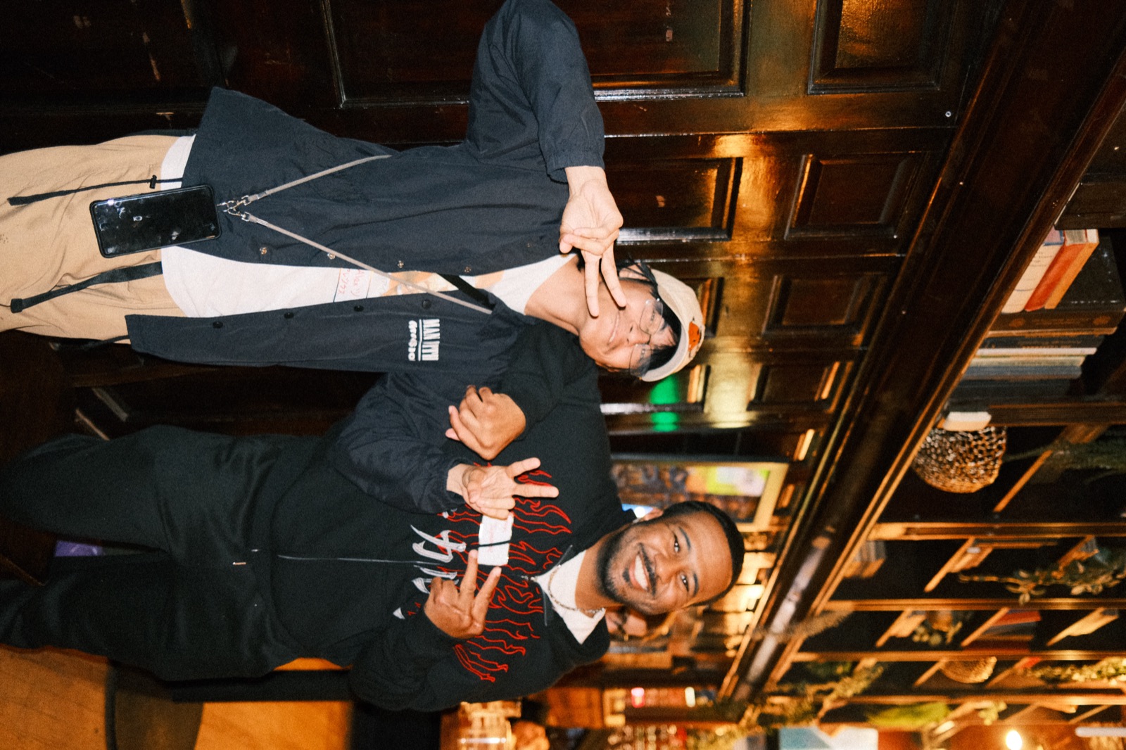 two guys mid-laugh, arms linked, double peace signs