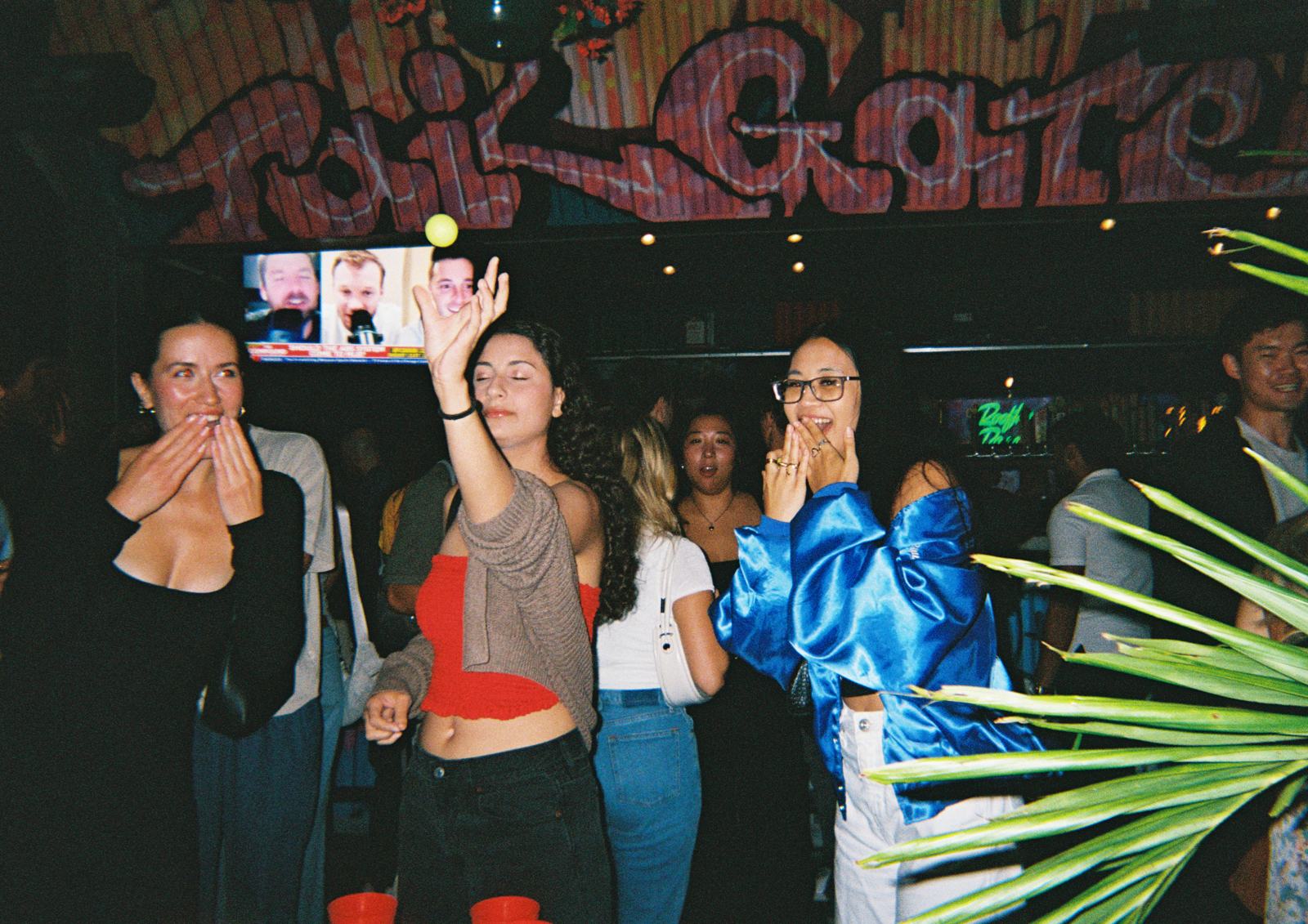 mid-toss over the pong table at arcade-bar night — the ball hanging in the air